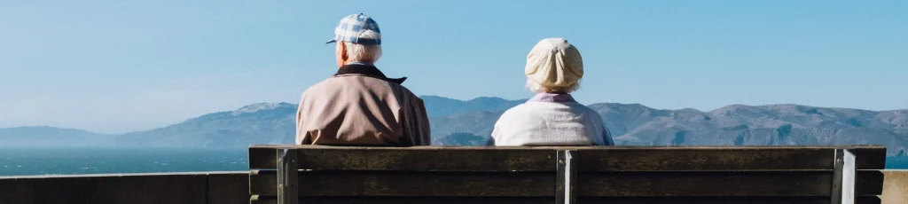 高齢の夫婦が天気の良い日にベンチに並んで座っている画像